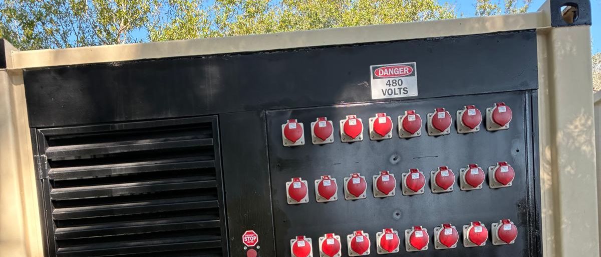 Front of a JD Power Packs unit: three rows of red 480 V reefer
                receptacles under a DANGER 480 VOLTS sign, with an emergency stop
                button and ventilation louvres.