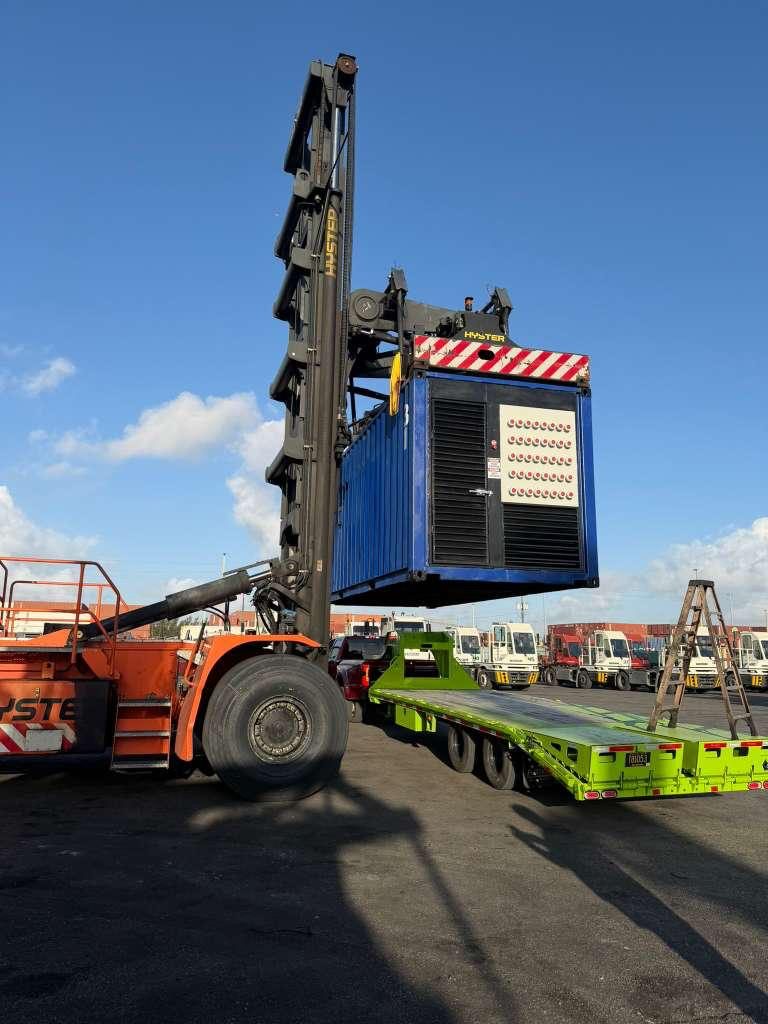 A containerized generator lifted by a reach stacker onto a lowboy
                  trailer at a container terminal.