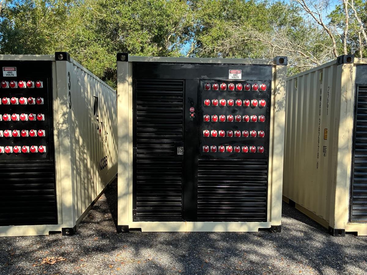 Three JD Power Packs containerized generator units lined up in the
                  yard, each with a bank of red 480 V reefer receptacles on its front panel.