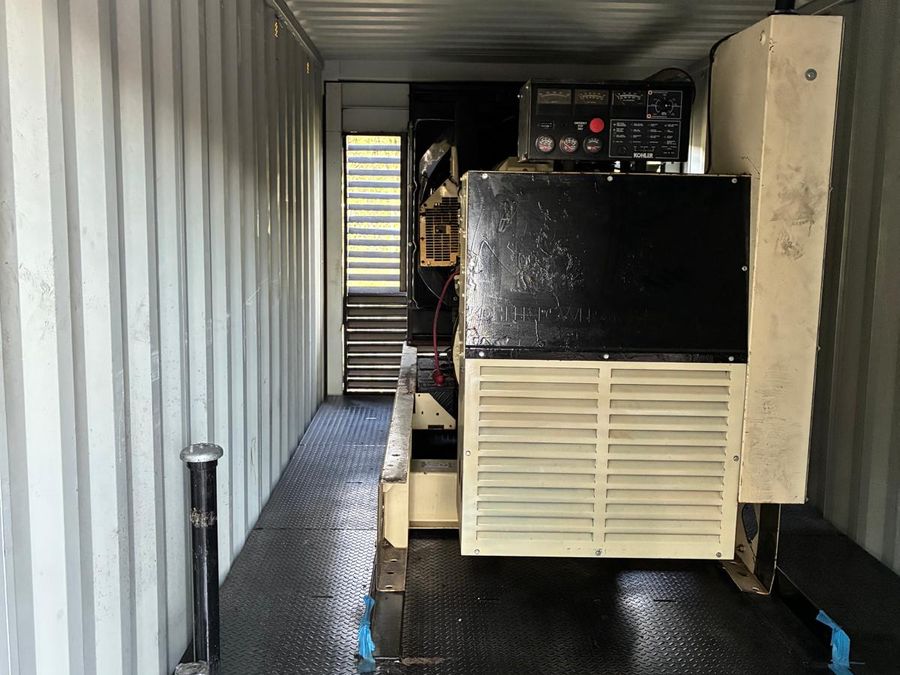 Cream-coloured generator enclosure inside a container, with its
                    control panel on top and a steel checker-plate floor.